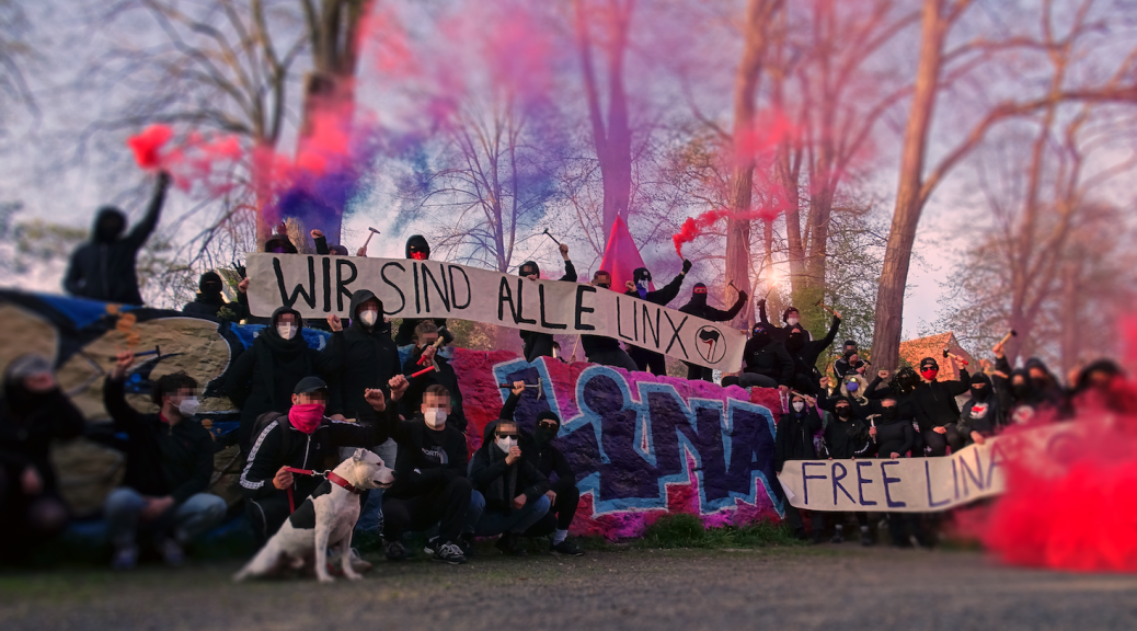 Antifaschist:innen vor einem Graffiti mit dem Text "Lina" mit Pyro und Rauchtöpfen in lila und rot. Auf den Tapeten steht "Wir sind alle Linx" und "Free Lina".